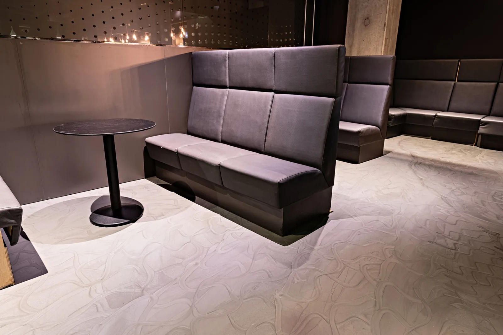 Lounge s čalúnenými lavicami na svetlej liatej podlahe s kresbou ťahov.